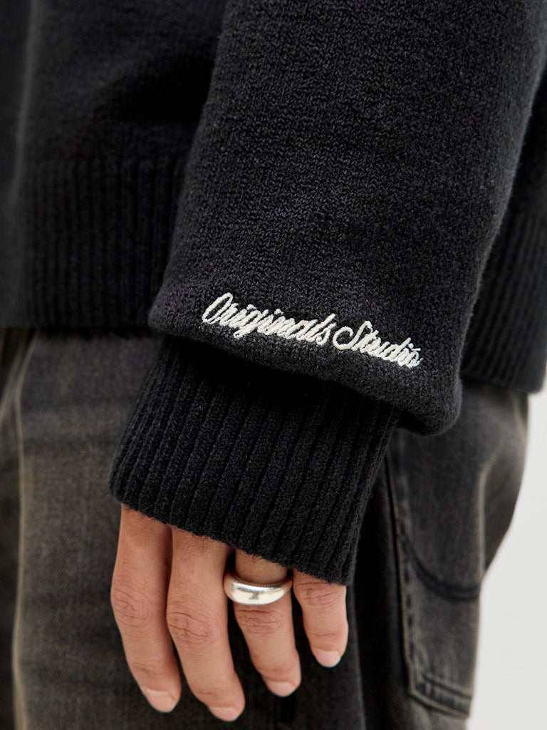 Black sweater with 'Originals Studio' embroidery on sleeve, worn by a person.