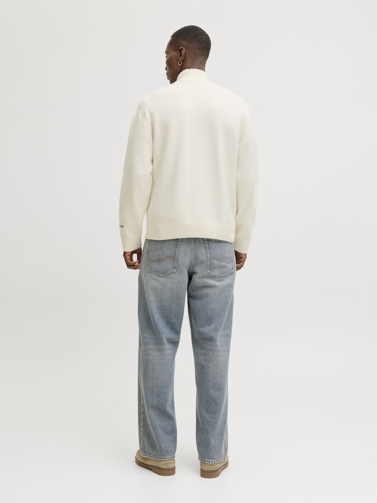 Person wearing a cream sweater and light blue jeans on a white background