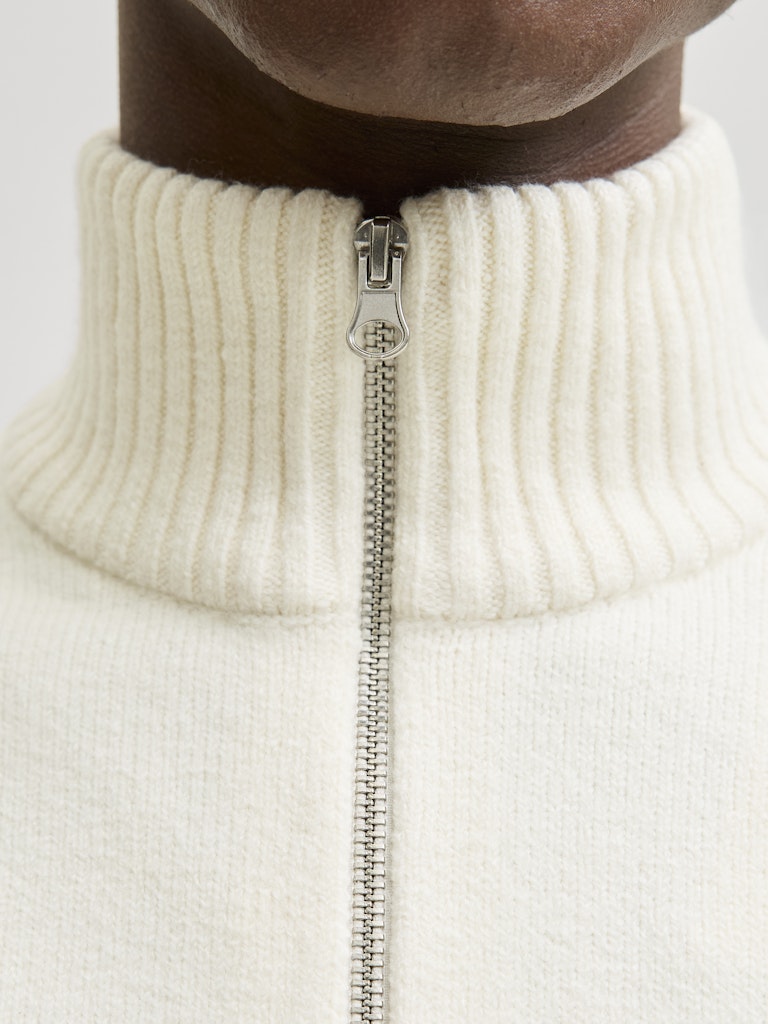 Close-up of a person wearing a cream-colored zip-up sweater with a zipper detail.