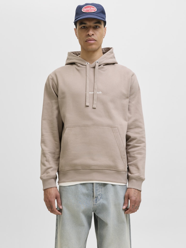 Person wearing a beige hoodie and blue cap on a plain background