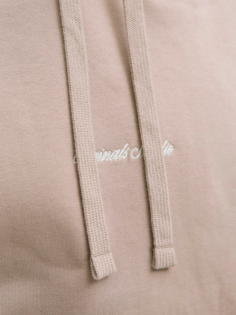 Close-up of a beige hoodie with a brand logo on the hood.