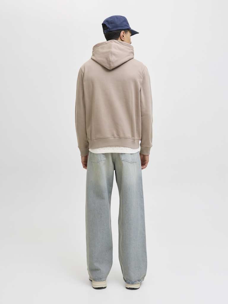 Person wearing a beige hoodie and light blue jeans on a white background-Back view