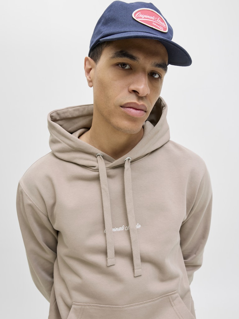 Person wearing a beige hoodie and navy cap with a red logo on a white background