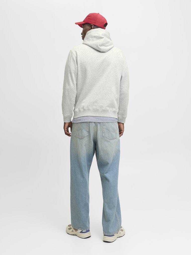 Person wearing a gray hoodie, light blue jeans, and a red cap on a white background