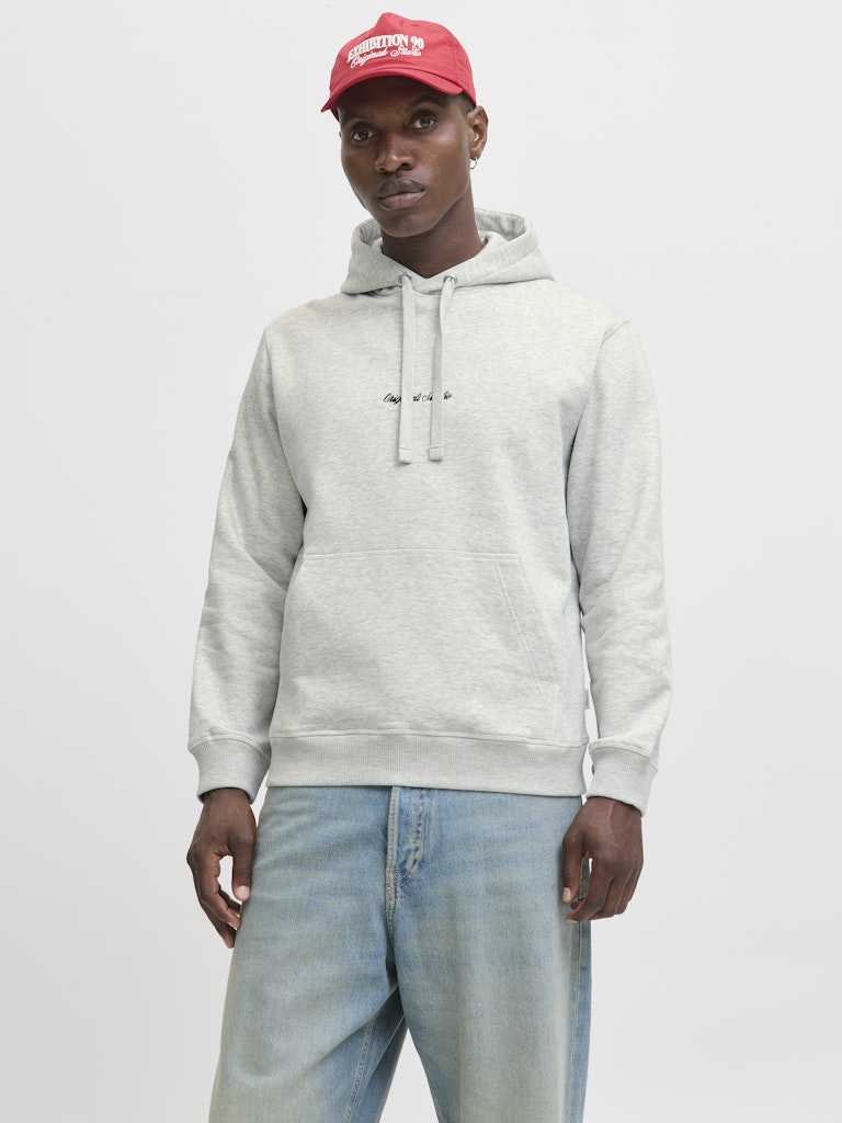 Man wearing a gray hoodie and light blue jeans with a red cap on a white background