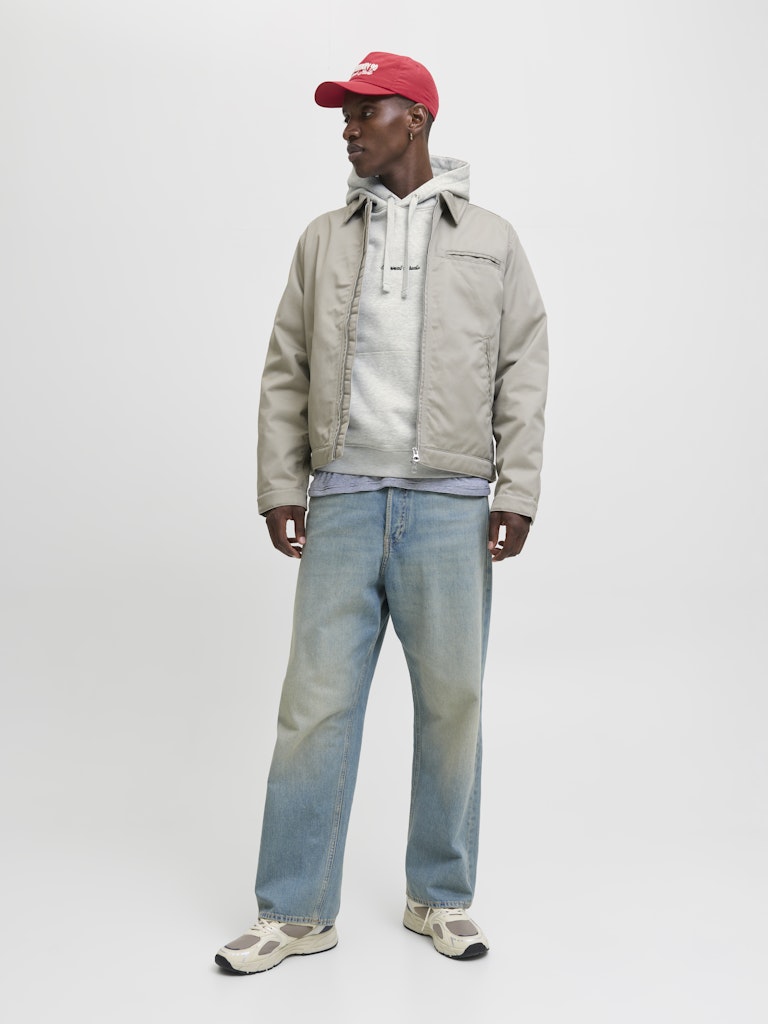 Person wearing a beige jacket, white hoodie, red cap, and light blue jeans on a white background