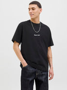 Person wearing a black t-shirt with white text and dark jeans on a light gray background