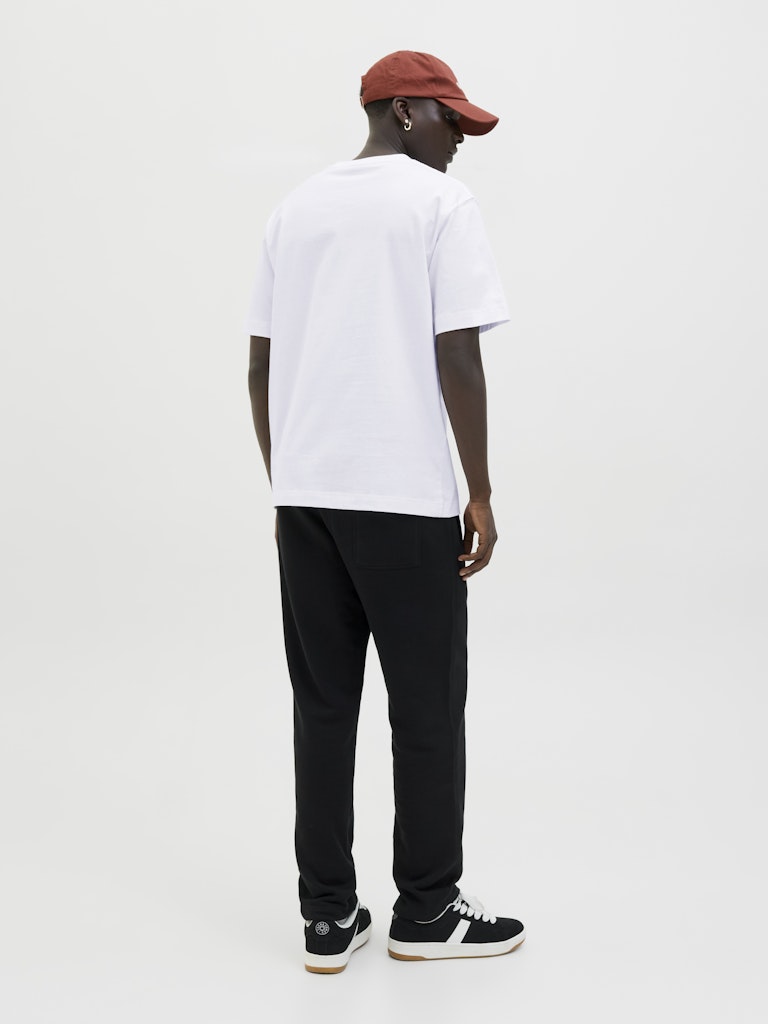 Person wearing a white t-shirt, black pants, and a red cap on a plain background