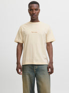 Man wearing a beige t-shirt with text and jeans on a white background