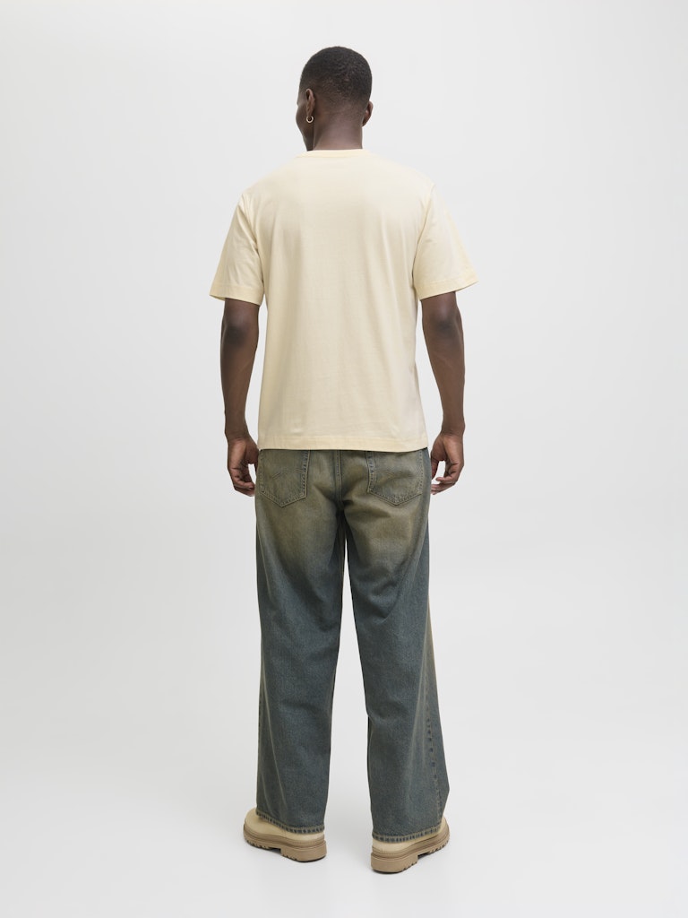 Person wearing a beige t-shirt and dark jeans on a white background