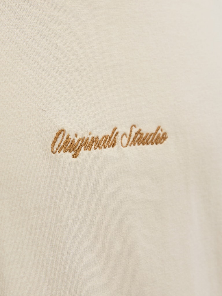 Embroidered text 'Originals Studio' on a beige tee
