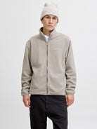 Person wearing a beige jacket and white beanie on a plain background