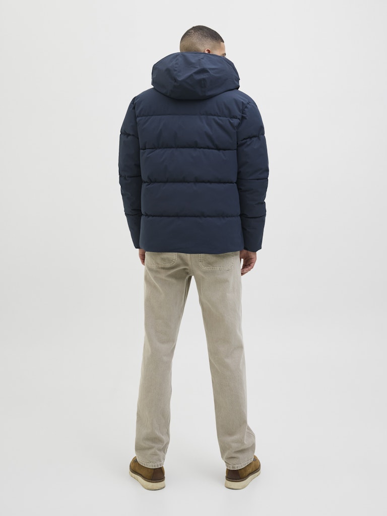 Person wearing a navy puffer jacket and beige pants on a white background