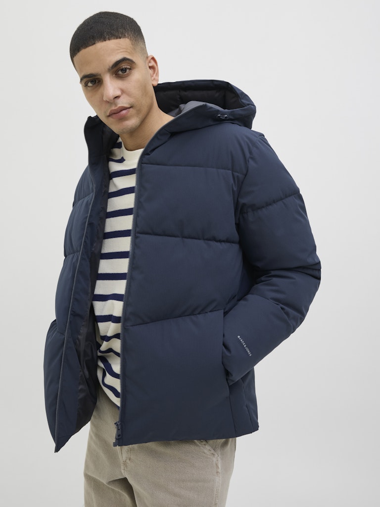 Man wearing a navy puffer jacket over a striped shirt on a white background