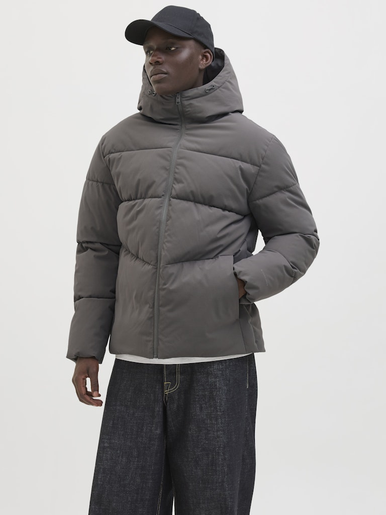 Person wearing a gray puffer jacket and black cap on a white background