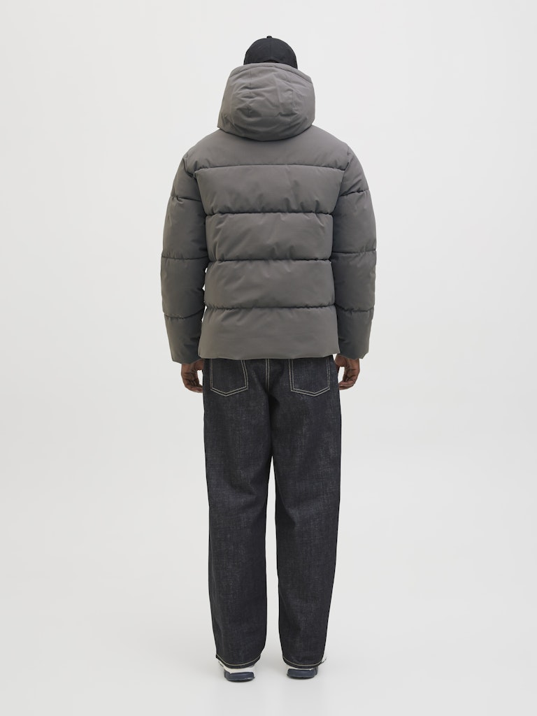 Person wearing a gray puffer jacket and dark jeans on a white background