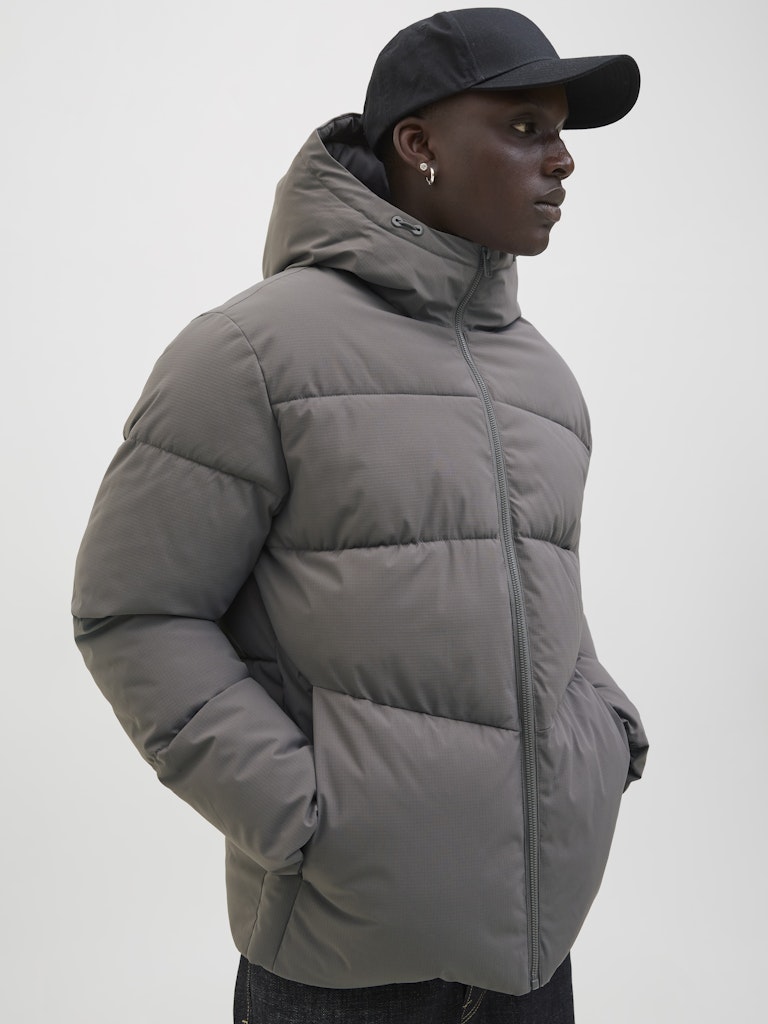 Person wearing a gray puffer jacket and black cap on a white background