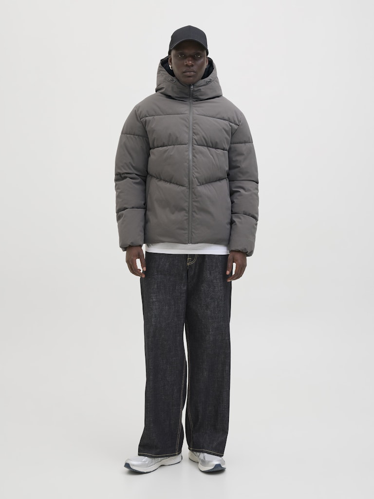 Person wearing a gray puffer jacket and dark jeans on a white background