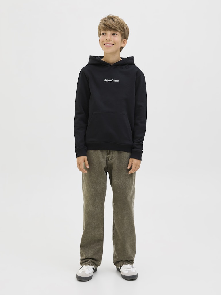 Young boy wearing a black hoodie with text and green pants on a white background