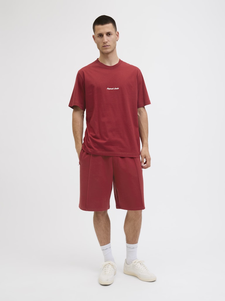 Man wearing a red t-shirt and shorts set with a white logo on a white background