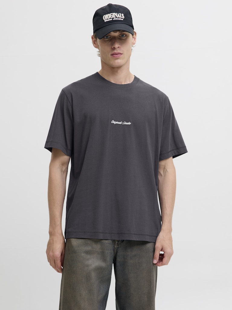 Person wearing a dark gray t-shirt with a logo and a black cap on a light gray background