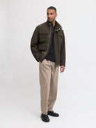 Man wearing a green jacket, black shirt, beige pants, and black shoes on a white background