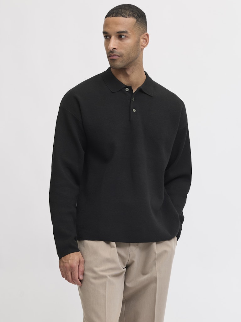 Man wearing a black long-sleeve polo shirt and beige pants on a white background