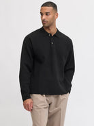 Man wearing a black long-sleeve polo shirt and beige pants on a white background