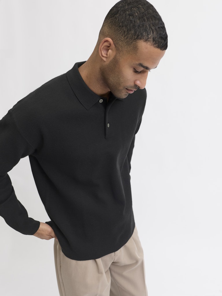 Man wearing a black long-sleeve polo shirt against a white background