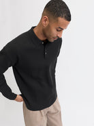 Man wearing a black long-sleeve polo shirt against a white background