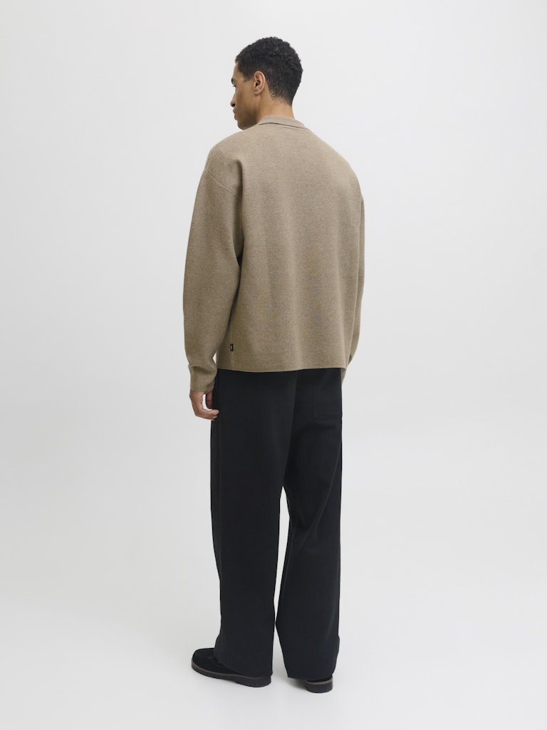 Man wearing a beige sweater and black pants on a white background