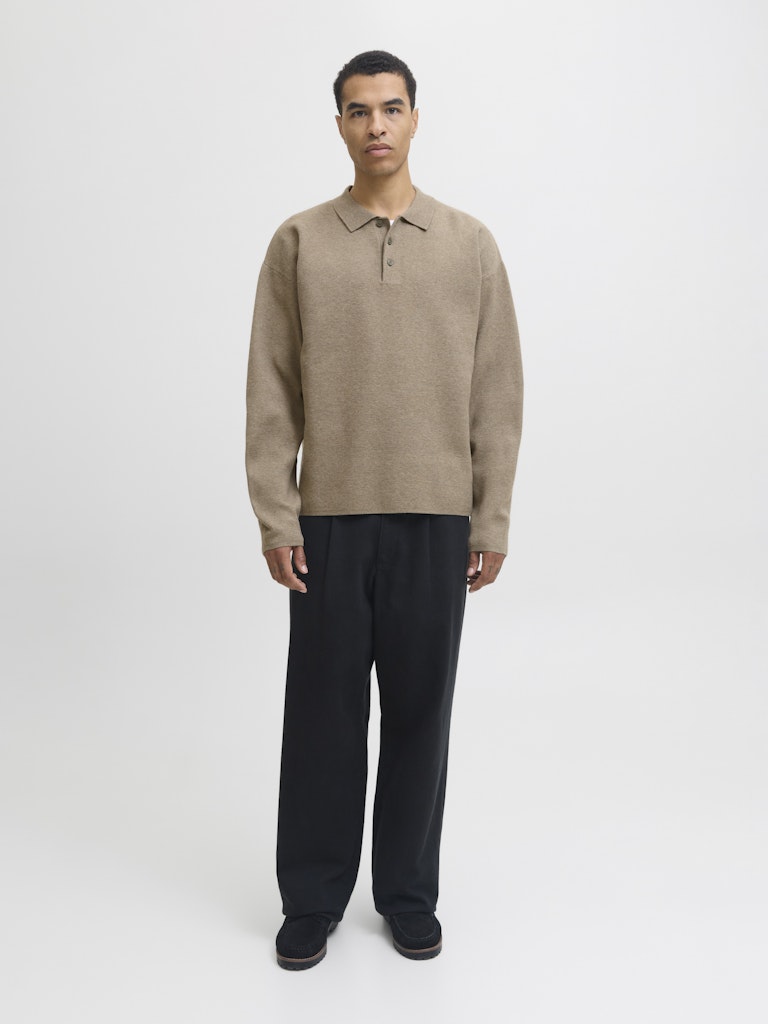 Man wearing a beige sweater and black pants on a white background