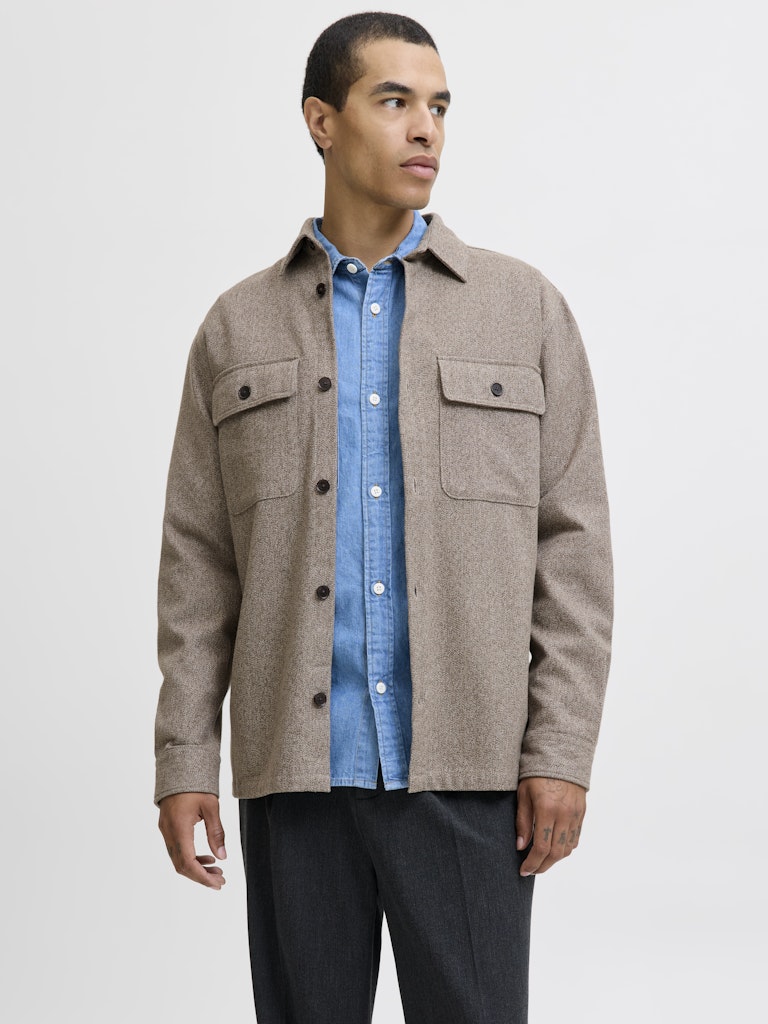 Man wearing a brown jacket over a blue shirt on a light gray background