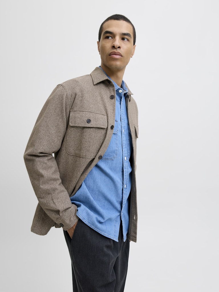 Man wearing a brown jacket over a blue shirt on a white background