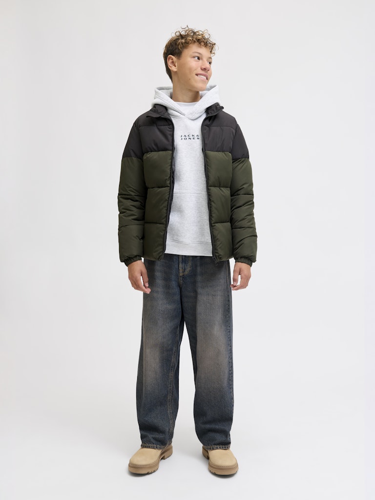 Person wearing a green and black puffer jacket, grey hoodie, and blue jeans on a white background
