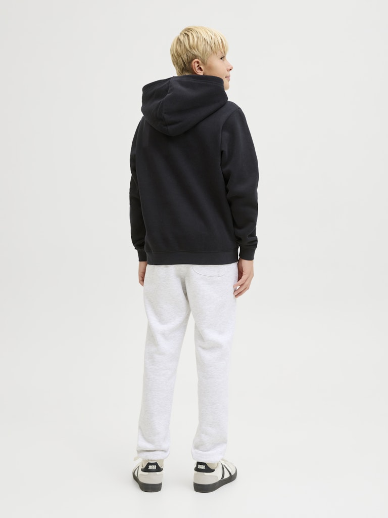Person wearing a black hoodie and white pants on a plain background