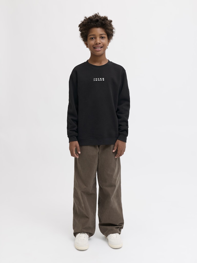 Person wearing a black long-sleeve shirt with text and brown pants on a white background