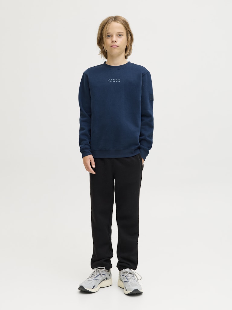 Person wearing a navy blue sweatshirt and black pants on a white background