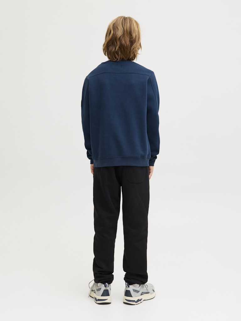 Person wearing a navy blue sweatshirt and black pants on a white background