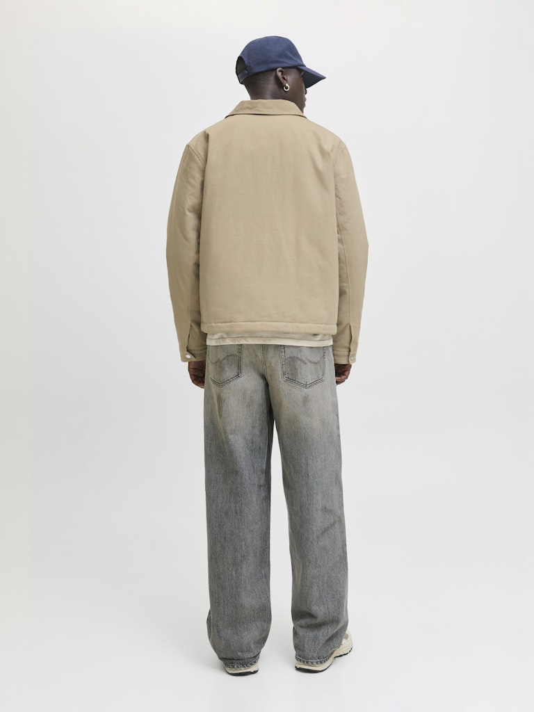 Person wearing a beige jacket and gray jeans from the back on a white background