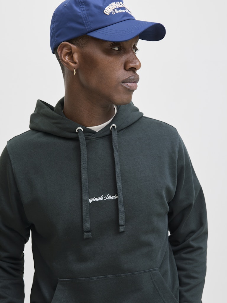 Person wearing a dark green hoodie and blue cap on a light gray background