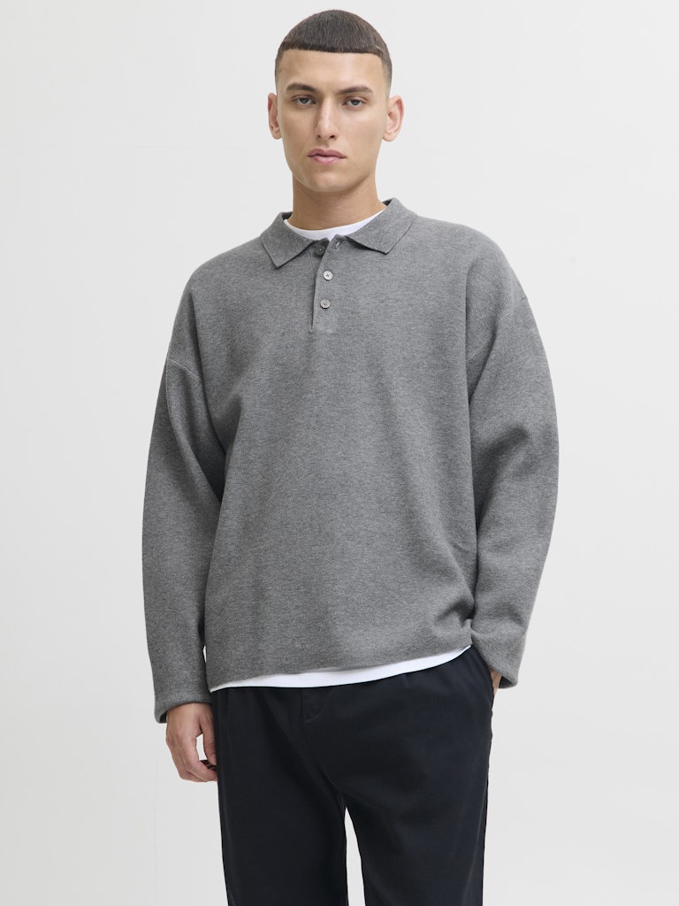 Man wearing a gray sweater over a white shirt with black pants on a light gray background