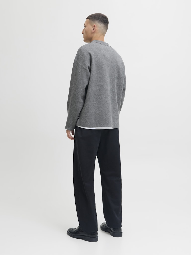 Man wearing a gray sweater and black pants on a white background