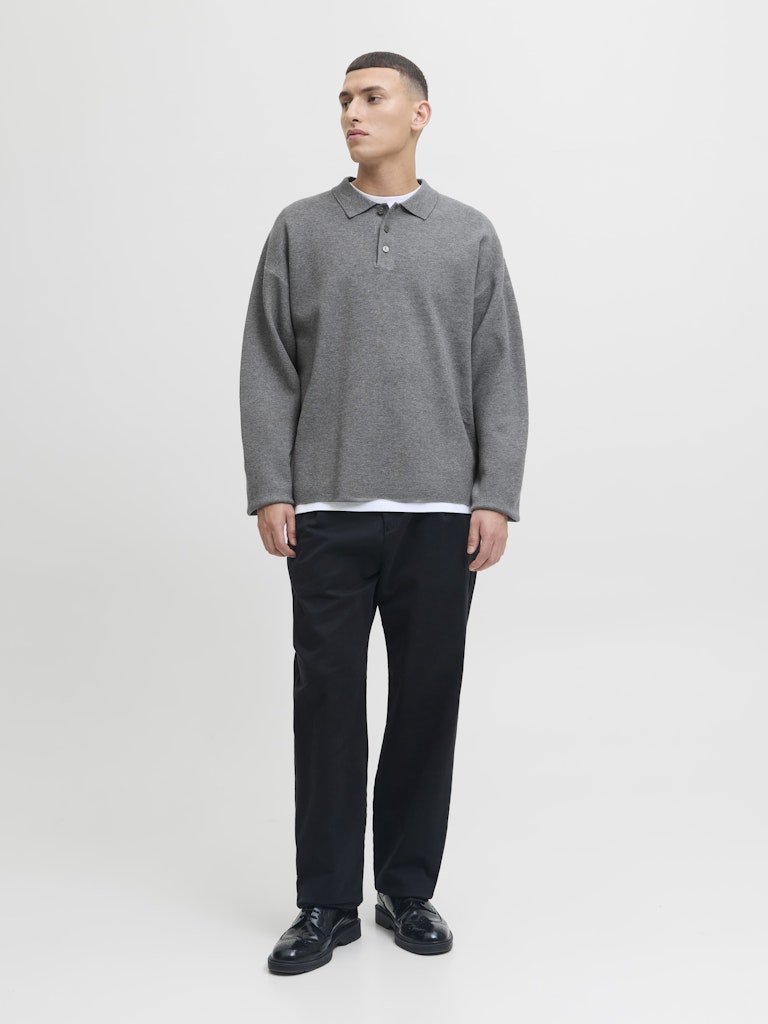 Man wearing a gray sweater over a white shirt with black pants on a white background