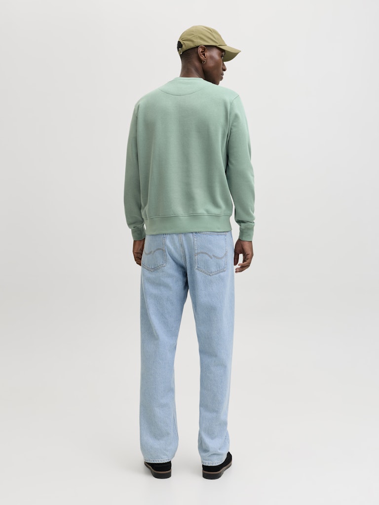 Person wearing a light green sweater and light blue jeans on a white background
