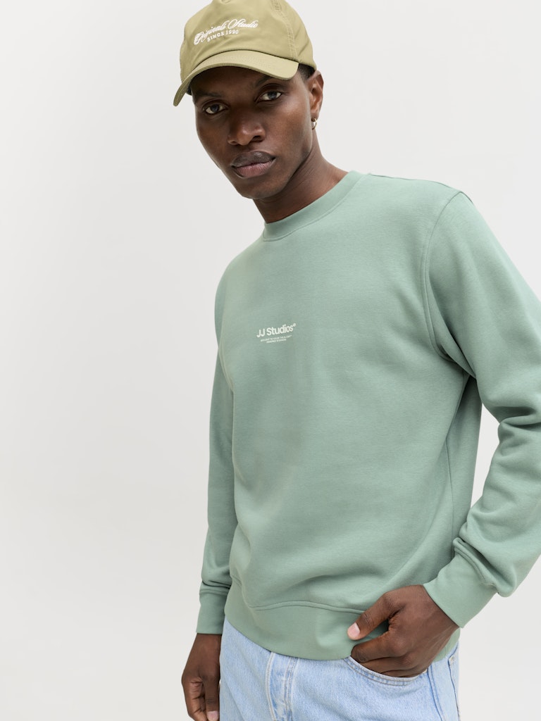 Person wearing a light green sweatshirt and beige cap on a white background