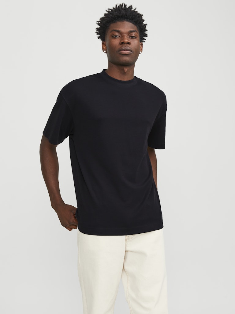 Man wearing a black t-shirt and white pants against a plain background