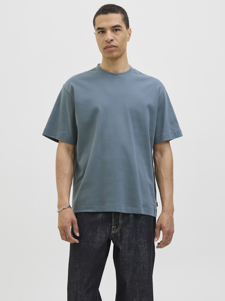 Person wearing a plain blue grey t-shirt and dark jeans on a light gray background