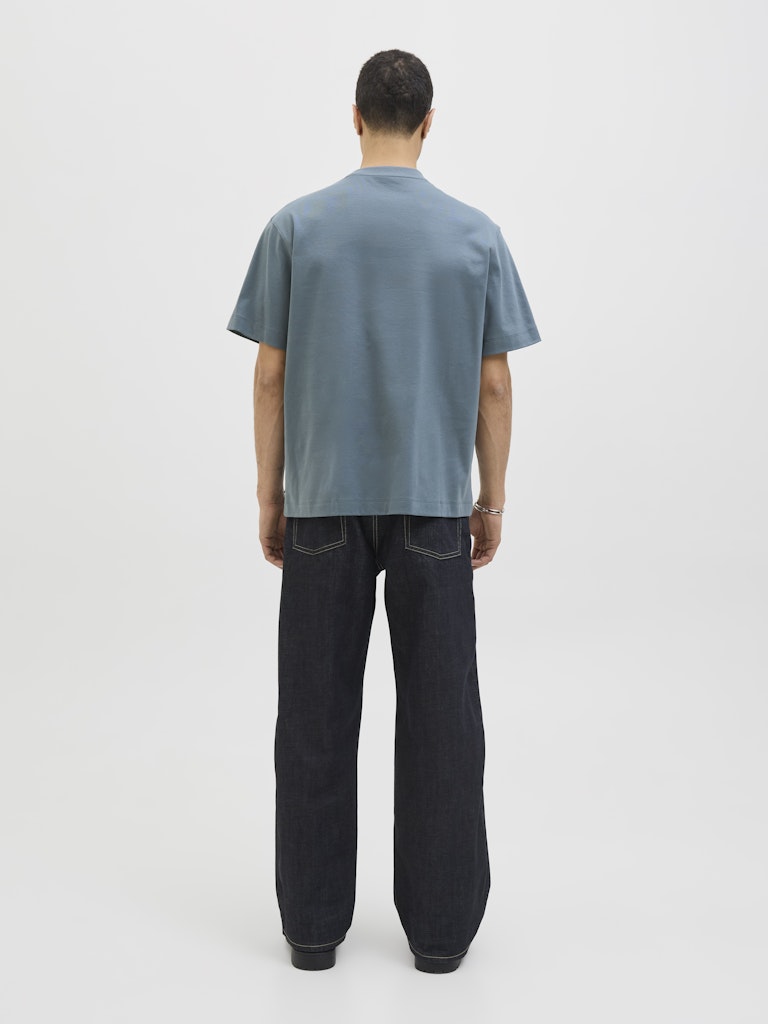 Person wearing a blue grey t-shirt and black pants on a white background