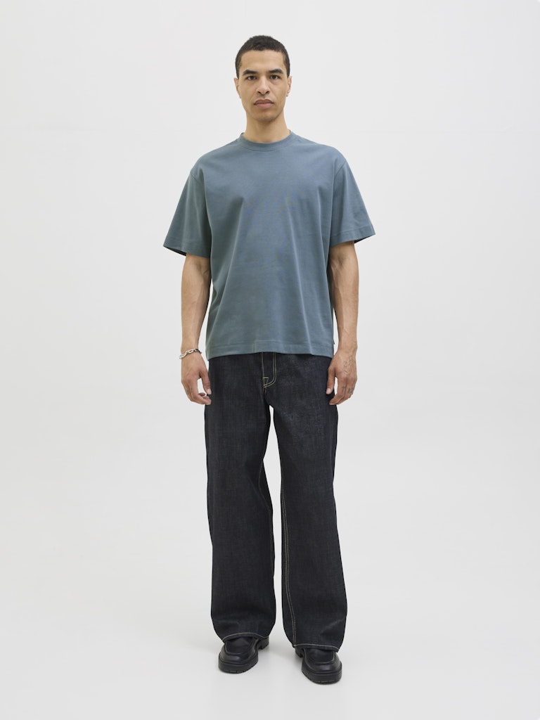 Man wearing a plain blue grey  t-shirt and dark jeans on a white background